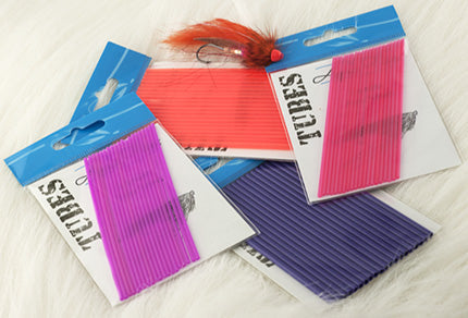 A display of brightly colored Aqua Flies Poly Tubes in pink, purple, and orange packaging, used for fishing tackle and lure customization, arranged on a light surface.