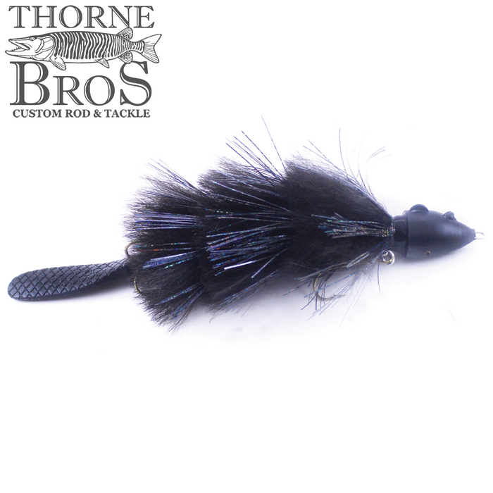 Black fishing lure with a textured tail and feathered body featuring iridescent dark fibers, designed for musky fishing, labeled Baby Beaver - Lake Edition by Thorne Bros.