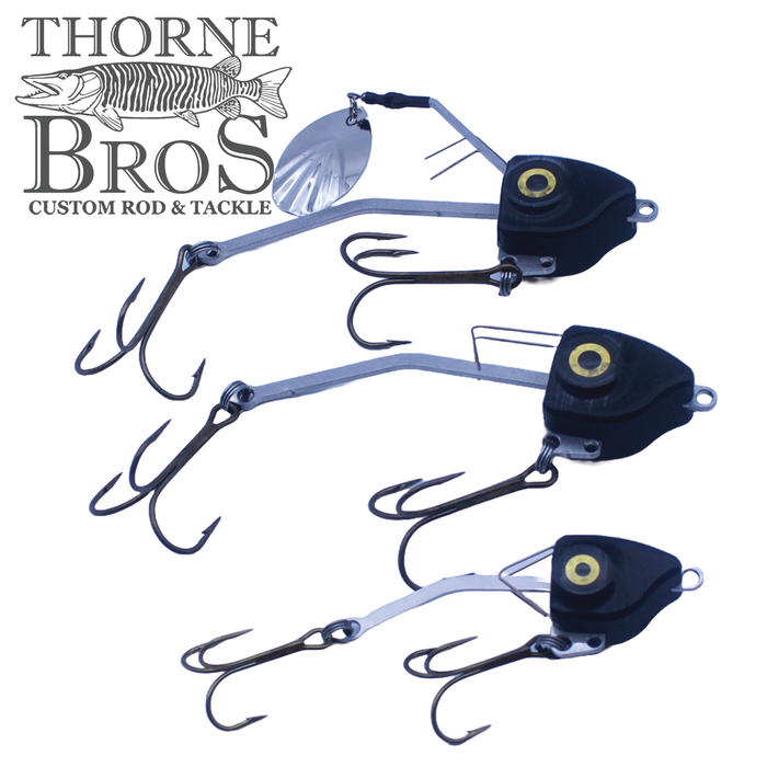 Three Barnestorm Baits X-Former fishing lures in small, medium, and large sizes with black bodies, yellow eye details, silver spinner blades, and multiple treble hooks arranged on a white background.