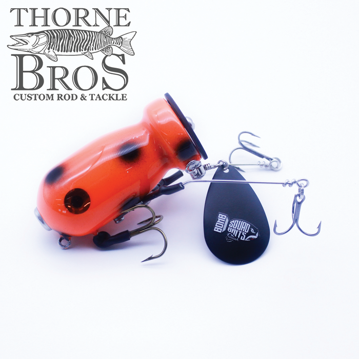 Close-up image of an orange and black fishing lure with multiple treble hooks and a black spinner blade featuring the Bomb Squad C-4 Flap Tail logo, displayed against a white background with the Thorne Bros Custom Rod & Tackle logo.