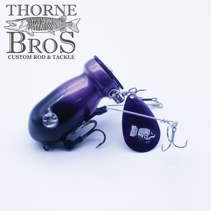 Bomb Squad C-4 Flap Tail fishing lure in dark purple with metal spinner blade and multiple sharp treble hooks, designed for musky fishing tackle from Thorne Bros.