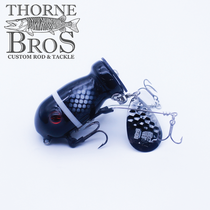 Bomb Squad C-4 Flap Tail fishing lure in black with white accents featuring dual treble hooks and a silver spinner blade, designed for musky fishing and heavy freshwater tactics.