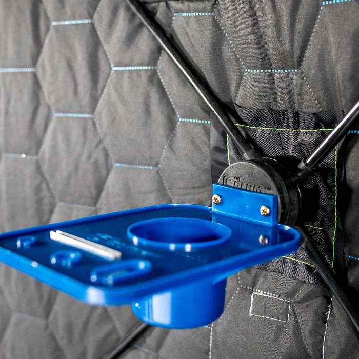 Close-up of a blue Clam ClamLock Hub Shelf attached to a quilted black fishing shelter wall, featuring multiple compartments for organizing fishing tackle and accessories.