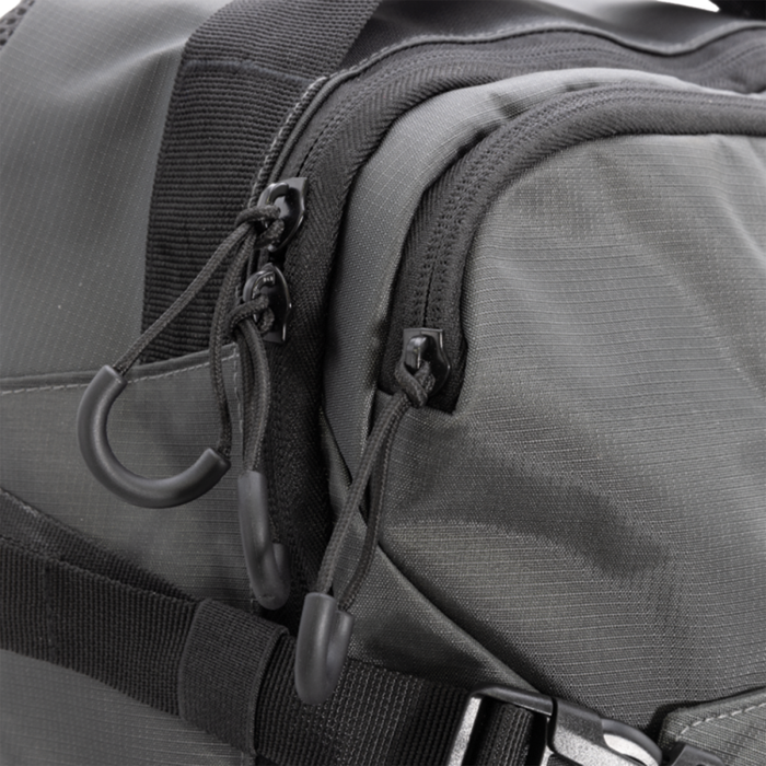 Close-up view of a gray Clam Slim Backpack made from durable ripstop fabric, featuring multiple zippered compartments with pull cords and adjustable straps for secure fishing tackle storage.