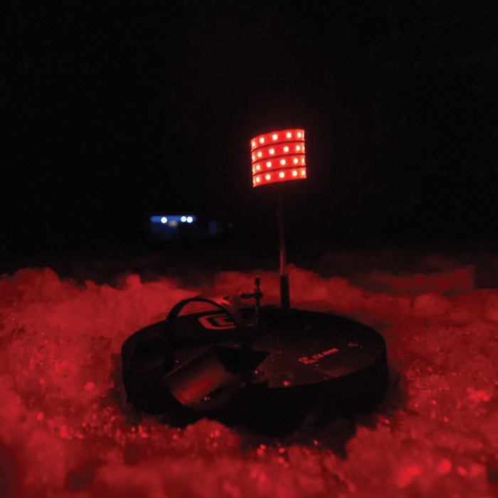 Clam Watchtower Lighted Tip-Up glowing red on ice at night, designed for ice fishing with a visible illuminated flag for easy bite detection in low light conditions.