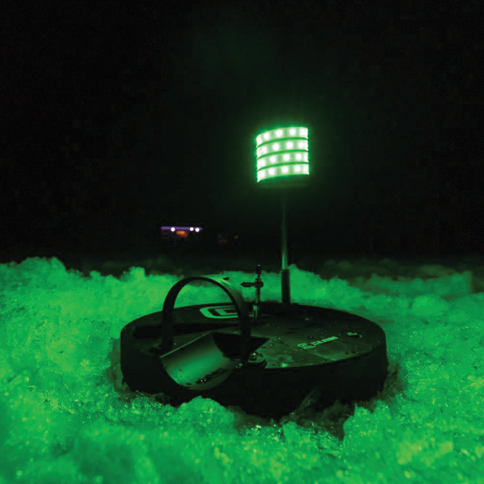 Clam Watchtower Lighted Tip-Up with bright green LED light mounted on black base set in ice, designed for enhanced visibility during night ice fishing.