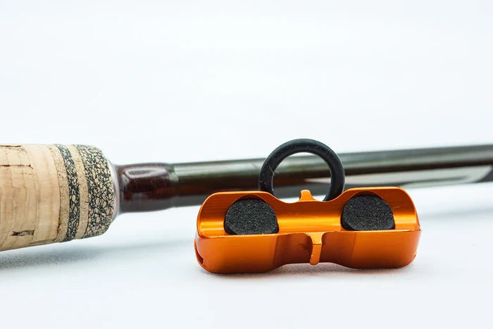 Cling Mag Grab Rod Rack in metallic orange designed to securely hold a fishing rod by gripping the base near the cork handle, shown against a white background.