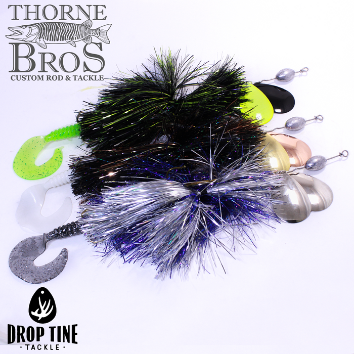 Three Drop Tine Base Jumper fishing lures with shiny, colorful tinsel skirts and curved soft plastic tails in green, white, and gray, each attached to weighted metal spinner blades.