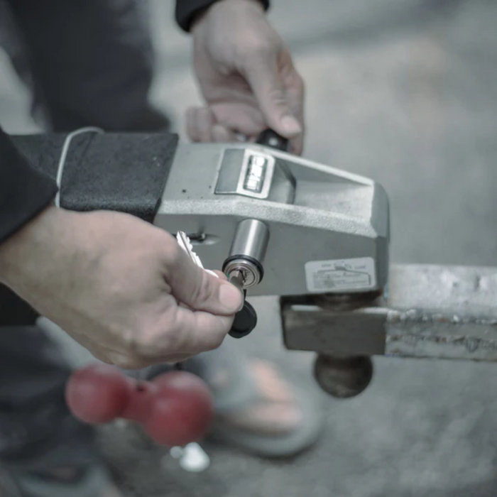 Person inserting key into a silver DuraSafe Coupler Lock 3" Pin installed on a metal hitch for securing a trailer or equipment connection.