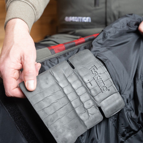 Close-up of a person holding a black insulated interior glove attached to the Eskimo Expedition Bib - Men's, showing padded waterproof fabric designed for warmth and durability in cold fishing conditions.
