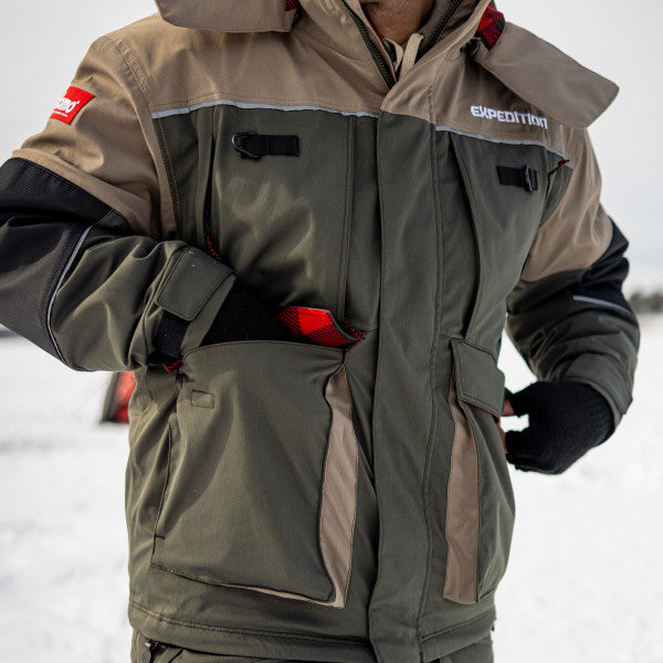 Close-up of a person wearing the Eskimo Expedition Jacket - Men's in olive green and tan, with multiple zippered pockets and insulated fabric, suitable for cold weather fishing conditions.
