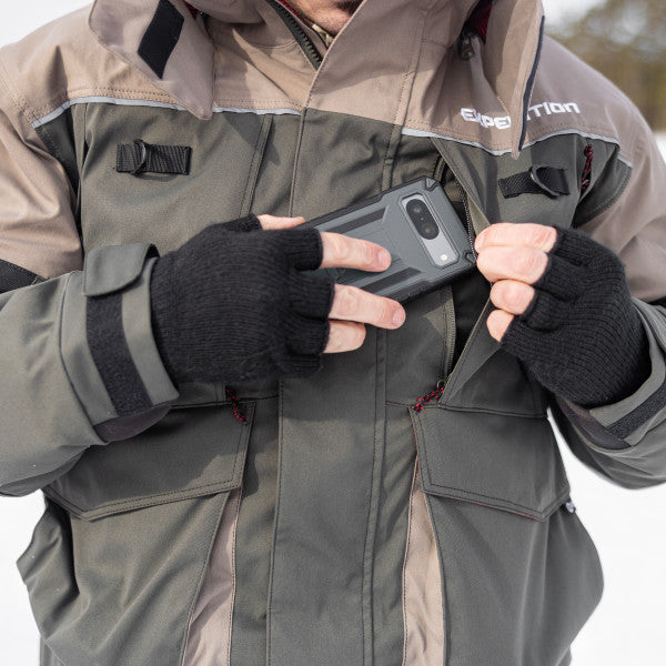 Man wearing Eskimo Expedition Jacket - Men's in gray and tan colors, using hands with black fingerless gloves to place a phone in the chest pocket outdoors.