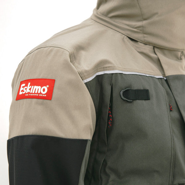 Close-up of the Eskimo Expedition Jacket - Men's showcasing durable beige and dark green fabric with a red Eskimo logo patch on the shoulder, designed for cold weather fishing.