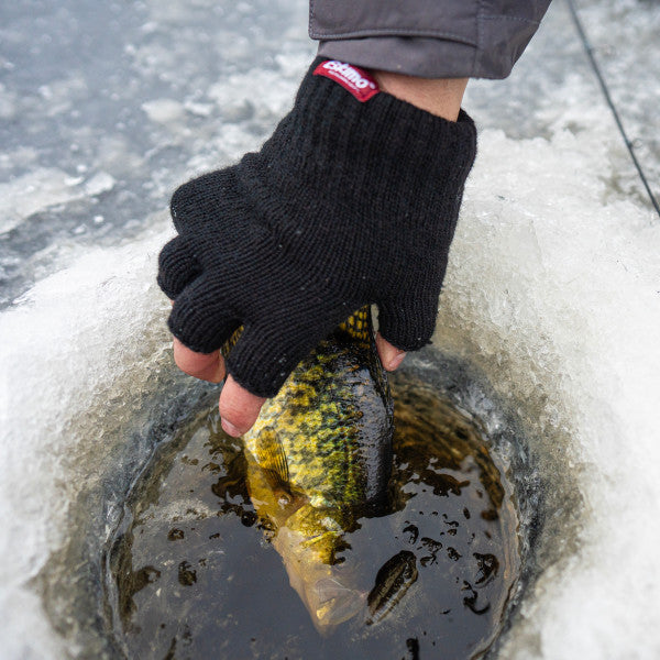Person wearing a black Eskimo Fingerless Wool Glove holding a yellow and black fish through an ice fishing hole on frozen water.