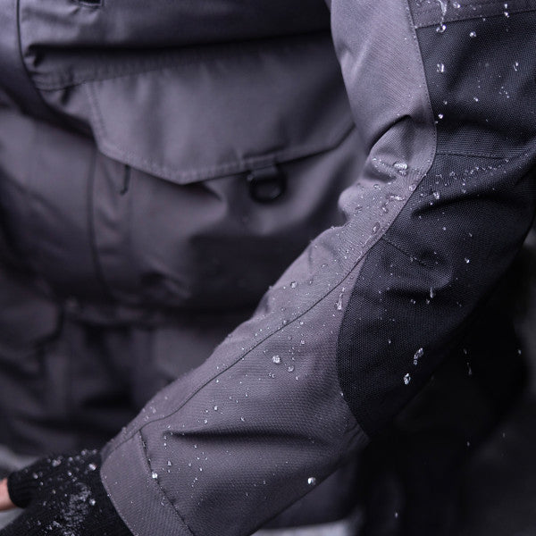 Close-up of water-resistant fabric on the sleeve of the Eskimo Roughneck Jacket - Men's, showing dark gray and black durable material with water beading on the surface.