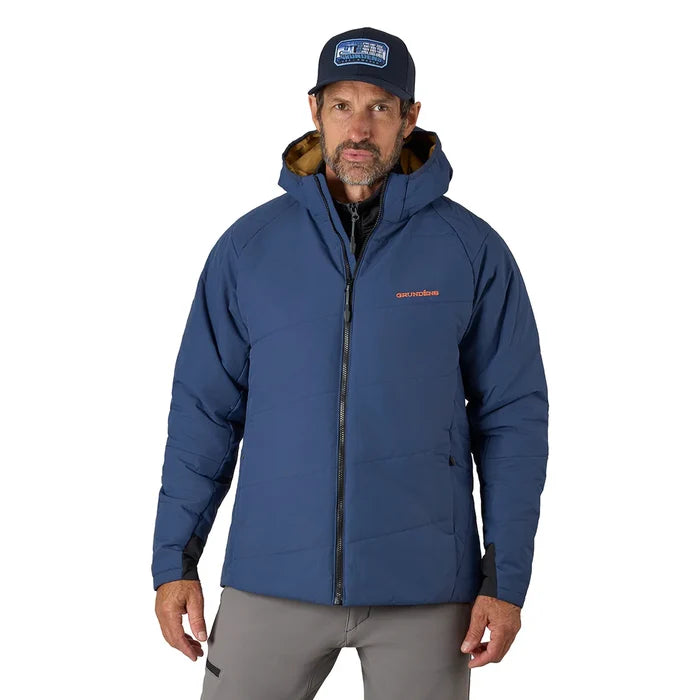 Man wearing a blue Grundens Turbulence Insulated Hoodie with a front zipper and hood, paired with gray pants and a dark blue cap, suitable for cold weather fishing activities.