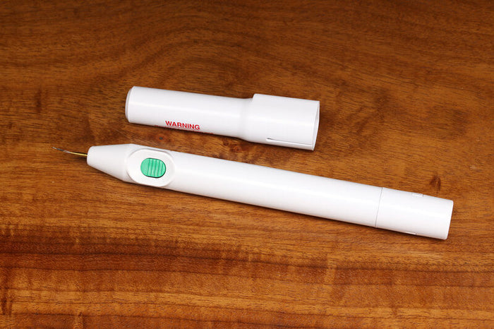 Hareline Cautery Tool, a white pen-shaped fishing tackle accessory with a green slider button and removable protective cap, displayed on a wooden surface.