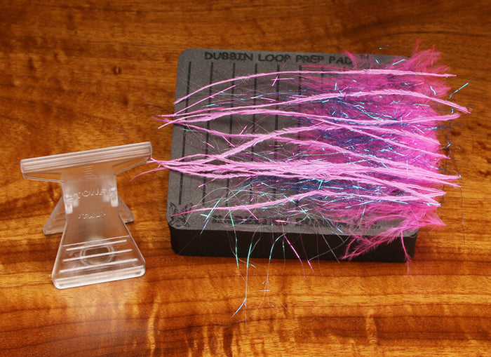 Hareline Dubbing Loop Prep Pad Kit showing a black foam pad with multiple pink and purple synthetic dubbing fibers and clear plastic clip, used for fly fishing tackle preparation.