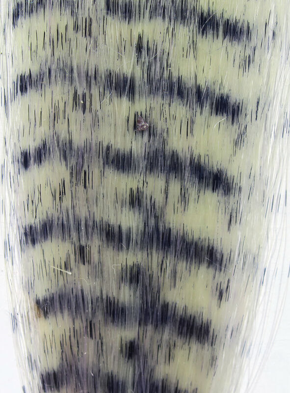 Close-up image showing a pattern resembling natural grizzly feathers in muted beige and black tones, representing Hareline Grizzly Fibre used in fly fishing tackle.
