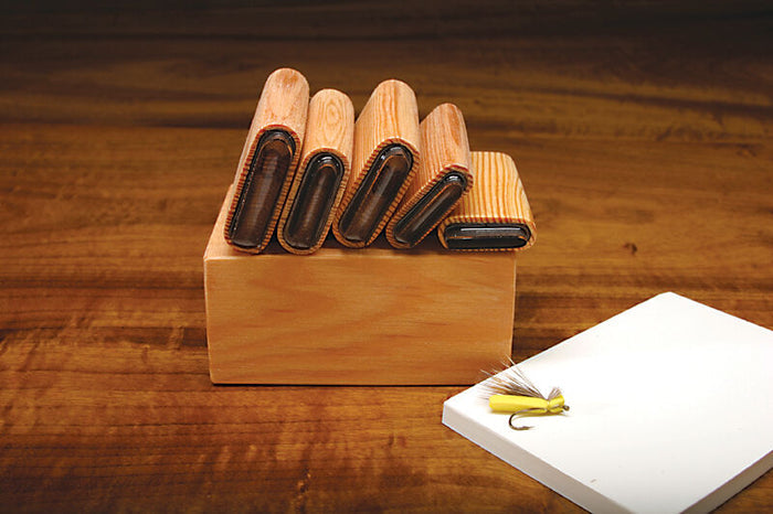Hareline Hopper/Caddis/Ant Foam Body Cutter with five wooden foam cutting templates arranged on a wooden base, shown next to a fly fishing lure on a white surface.