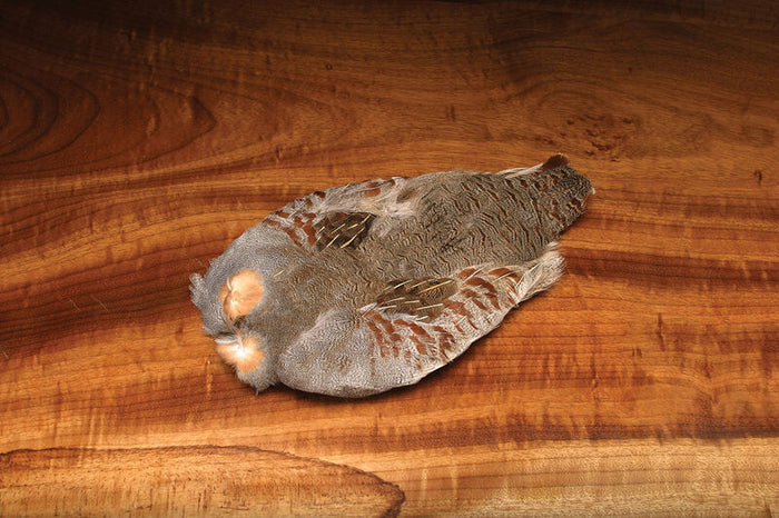 Hareline Hungarian Partridge Skin laid flat on a wooden surface, showing detailed grey and brown feather patterns used for fly fishing lure tying.