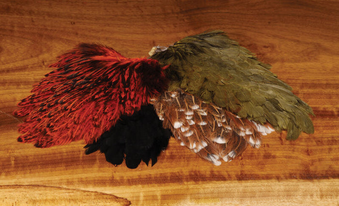 Hareline India Hen Back featuring a variety of natural red, olive, brown, and black feathers arranged on a wooden surface, ideal for fishing lure tying.