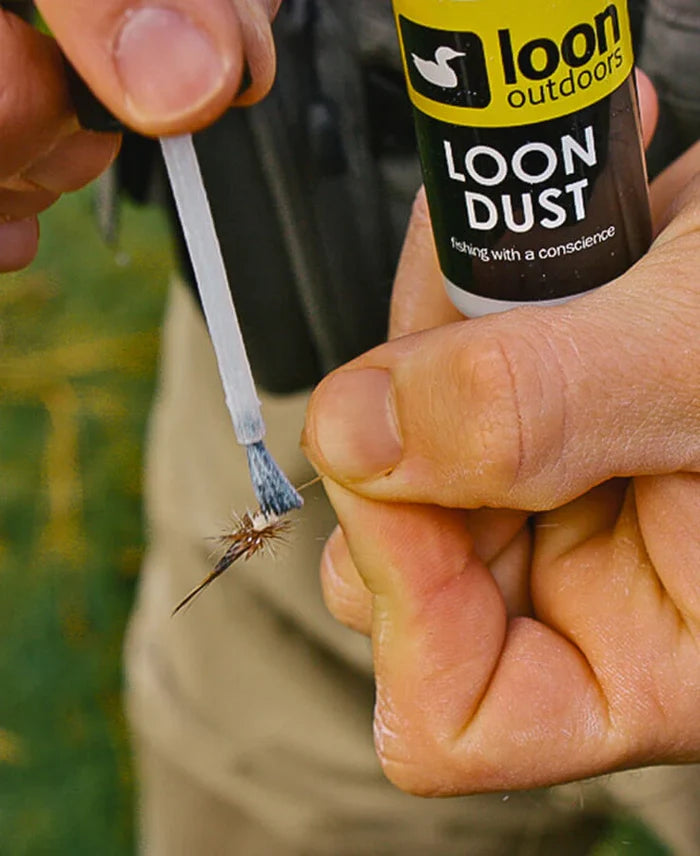 Close-up of hands applying Loon Dust with a small brush to a fly fishing lure, demonstrating preparation of fishing tackle for fly fishing.