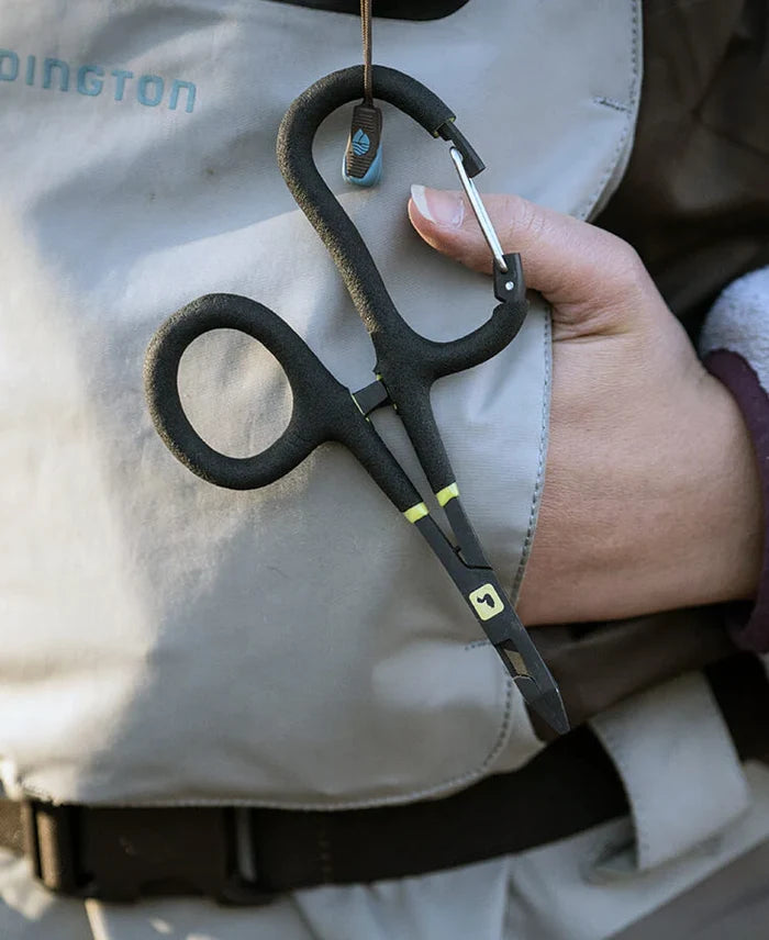 Loon Rogue Quickdraw Forceps with ergonomic black handle and cutting tip hanging from a carabiner attached to fishing vest, held by an angler's hand.