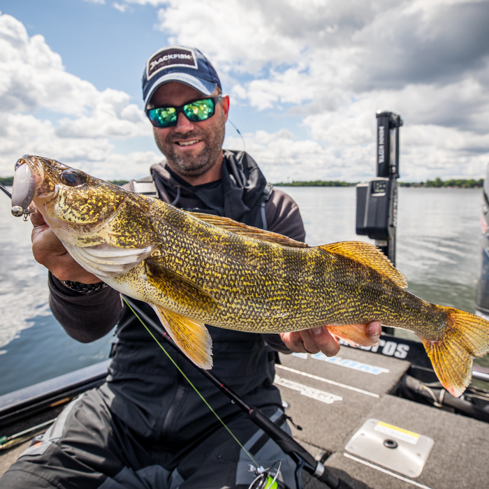 Man wearing sunglasses and a cap holding a large walleye fish on a boat, showcasing the Matt Johnson Outdoors - OW Walleye Rod *4 Week Build Time used for fishing on a lake under a partly cloudy sky.