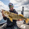Man wearing sunglasses and a cap holding a large walleye fish on a boat, showcasing the Matt Johnson Outdoors - OW Walleye Rod *4 Week Build Time used for fishing on a lake under a partly cloudy sky.