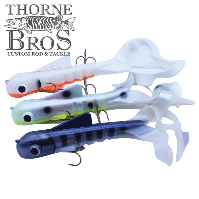 Three soft plastic fishing lures in white, green, and dark blue colors with curled tails and treble hooks, designed as Musky Innovations Double Dawg - Super Magnum (Pounder) for musky fishing.