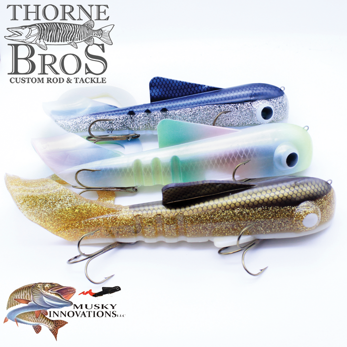 Three Musky Innovations TB Custom Ultra Dawg fishing lures in metallic blue, green, and gold with detailed eyes and treble hooks, displayed on a white background with Thorne Bros and Musky Innovations logos.