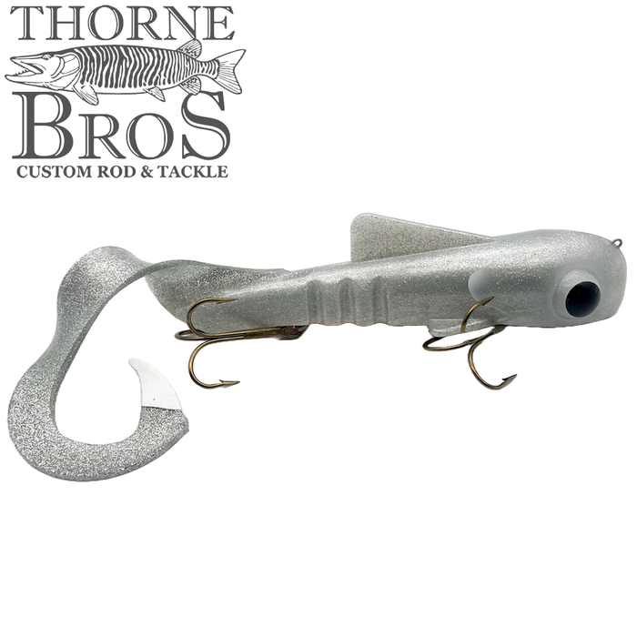 Musky Innovations TB Custom Ultra Dawg fishing lure in silver with a curly tail and two treble hooks, designed for musky fishing, shown against a white background.