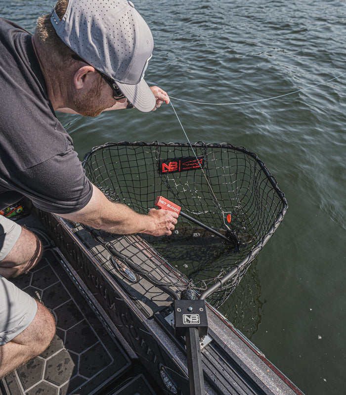 Man on boat using the Net Buddy DWF Hookout with a fishing net to assist in landing a fish over the side of the boat on a freshwater lake.