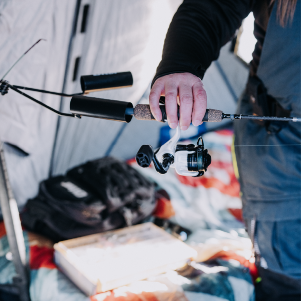Person holding a fishing rod secured in the black Otter QA Dual Rod Holder, designed for stable and organized fishing rod storage during ice fishing.