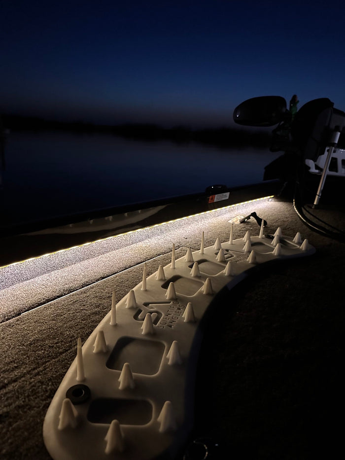 Scientific Anglers Launch Pad mounted on a boat deck at dusk, showing spiked design for secure fishing tackle storage with subtle LED strip lighting in the background.