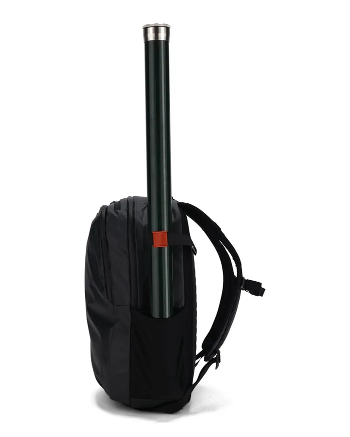 Simms Cam Strap securing a green fishing rod tube vertically on the side pocket of a black backpack designed for convenient transport of fishing tackle.