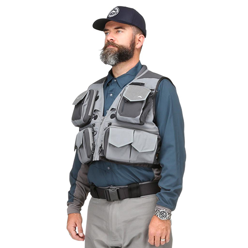 Man wearing a gray Simms G3 Guide Vest with multiple large front pockets over a blue long-sleeve shirt and gray pants, paired with a black belt and dark baseball cap.