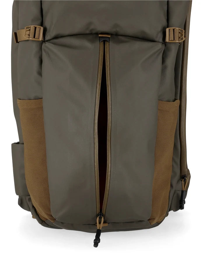 Close-up view of the front lower section of the Simms Headwaters Backpack in muted olive and tan tones, featuring a vertical zipper pocket and mesh side compartments designed for durable outdoor use.