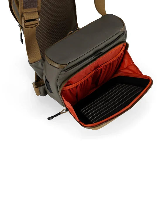 Simms Headwaters Chest Pack shown open with olive green exterior and bright orange interior featuring organized compartments and padded dividers for fishing tackle storage.