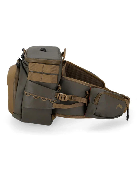 Simms Headwaters Hip Pack in muted green and brown with multiple zippered compartments, adjustable buckle strap, and mesh padding for comfortable fishing tackle storage.