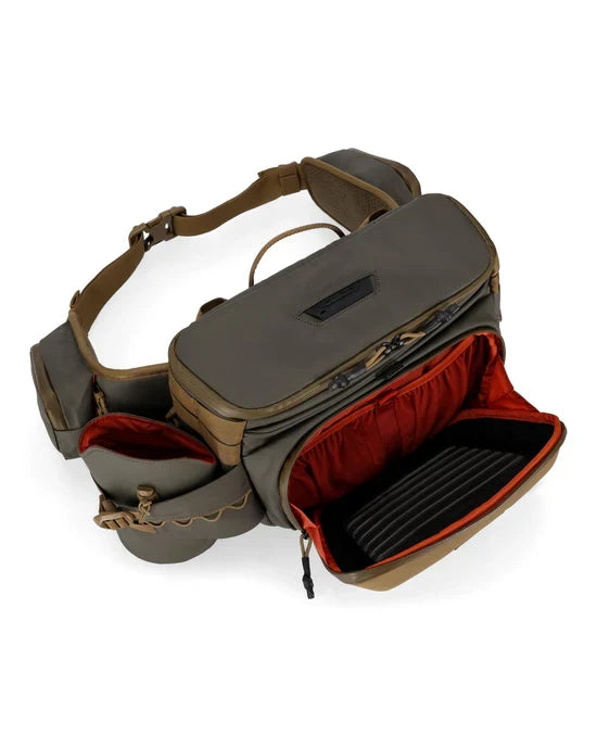 Simms Headwaters Hip Pack in olive and tan, showing multiple zippered compartments with red interior lining, designed for organized fishing tackle storage and comfortable wear.