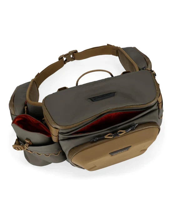 Simms Headwaters Hip Pack in earth tones with multiple zippered compartments and padded adjustable waist strap, designed for organized fishing tackle storage and easy access.