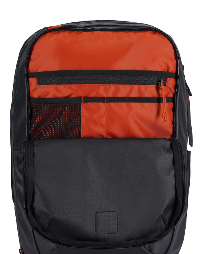 Simms Tailwind Backpack shown open with multiple interior compartments including a zippered pocket, mesh pocket, and organizer slots in orange and black fabric for fishing tackle storage.