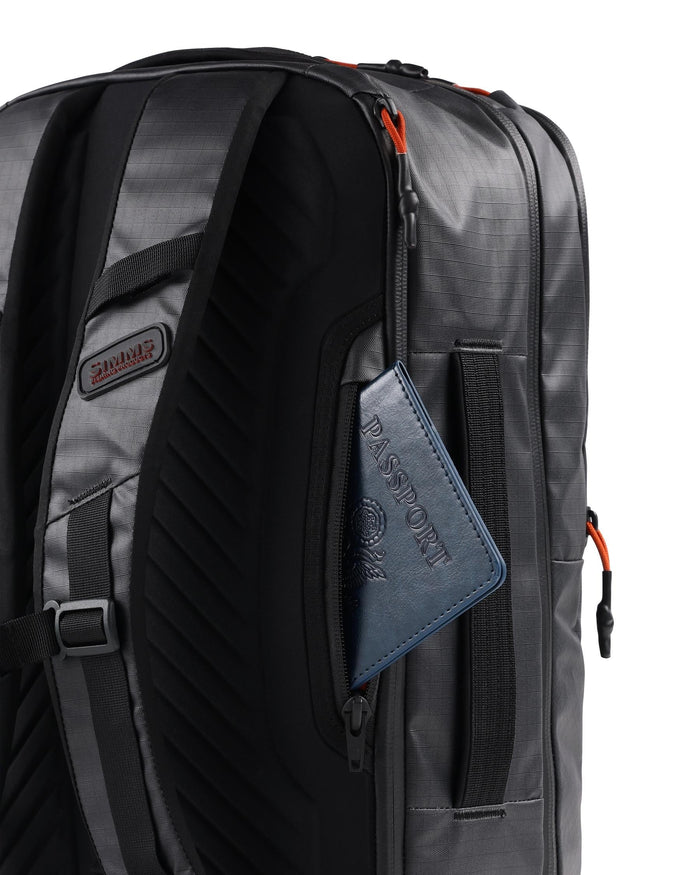 Simms Tailwind Backpack in black with padded shoulder straps, a zippered side pocket holding a blue passport, and durable water-resistant material, designed for fishing tackle storage.