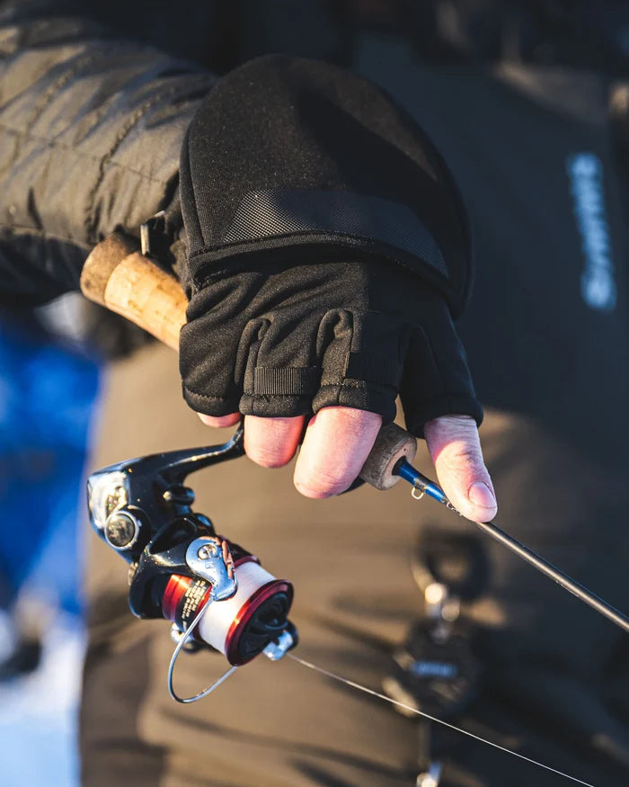 Close-up of a hand wearing black Simms Windstopper Foldover Mitt gripping a fishing rod and reel, showcasing the mitt’s foldover design and fishing functionality.