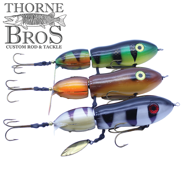 Three articulated fishing lures with treble hooks and vibrant finishes in green, brown, and black-and-white patterns, marketed as Snaggle Tooth Tackle Super Beast Prop Bait.