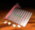 Clear plastic Stash Flash Pods organizer with multiple compartments, displayed on a wooden surface alongside pink and silver flash fibers used for fishing lure customization.