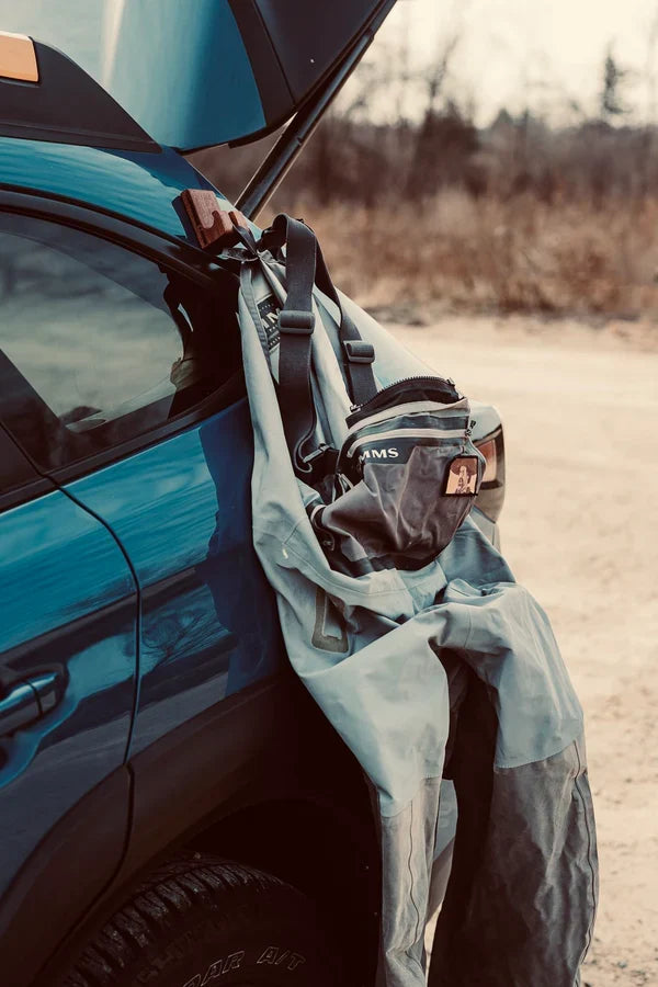 Temperance & Penn Gear Hook-Magnetic securing fishing waders to the side of a blue vehicle outdoors, demonstrating hands-free gear organization for anglers.