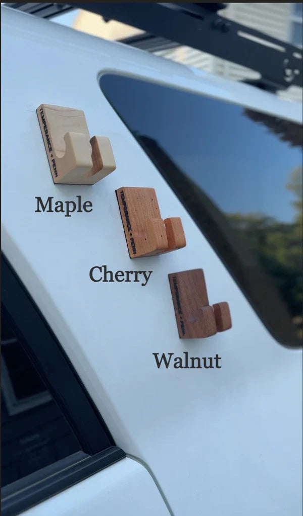 Three wooden Temperance & Penn Gear Hook-Magnetic fishing tackle holders in maple, cherry, and walnut finishes mounted on a vehicle surface for convenient gear storage.